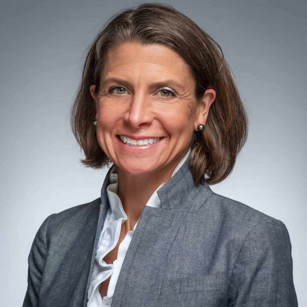 Bio photo of woman with chin length brown hair wearing a grey suit jacket with white shirt.